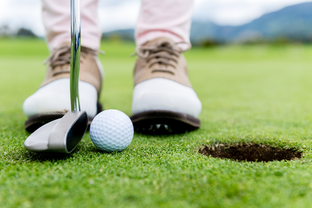 Golf player at the putting green hitting ball into a hole-1